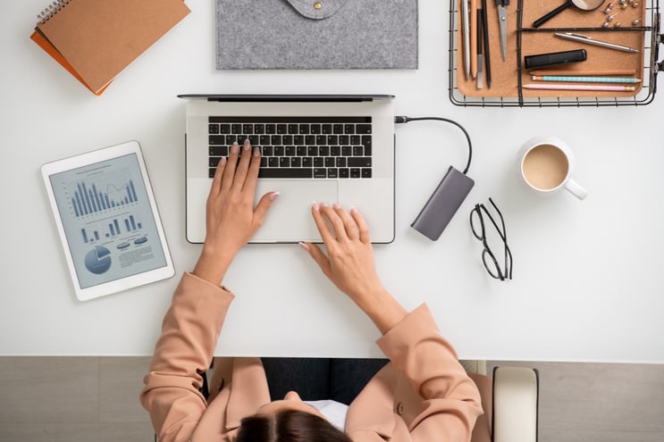 overview-young-elegant-businesswoman-sitting-by-desk-front-laptop-touching-keys-while-entering-new-data-networking